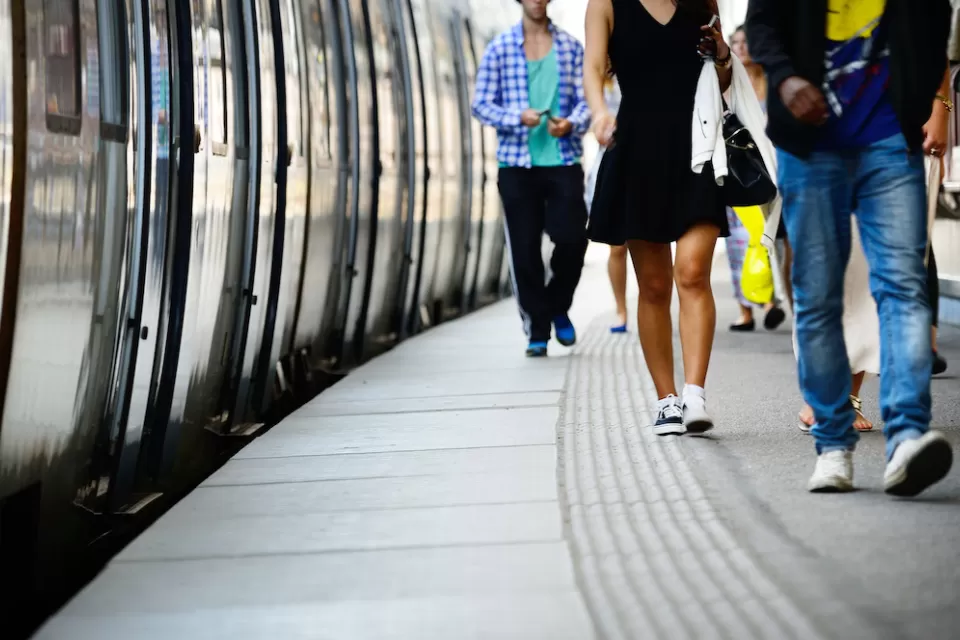 Low shot of side of subway or commuter train and passengers walking on platform next to it.